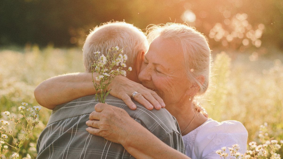 A senior couple embraces joyfully in a sunny meadow, capturing a moment of happiness and love.