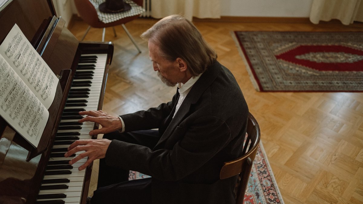 Senior man elegantly playing piano with music sheets in a warm, classic living room.