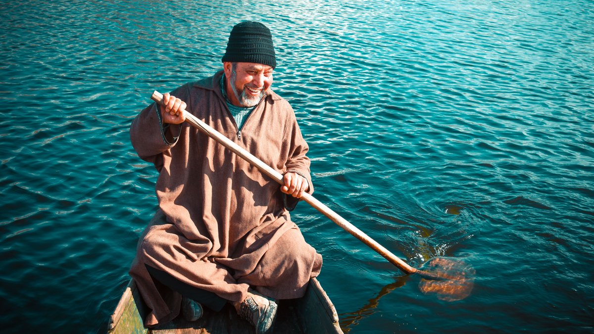 Senior man smiling while rowing a wooden boat on clear water, exhibiting joy and tranquility.
