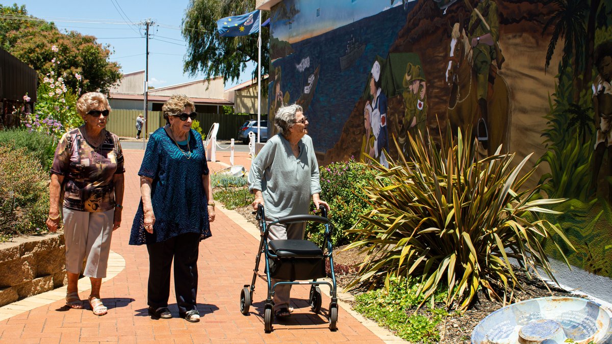 Three senior women enjoying a sunny walk by a vivid mural, capturing community and friendship.
