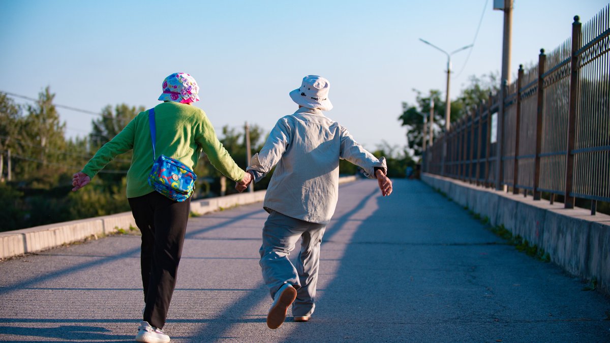 Elderly couple in colorful attire walking hand in hand on a sunny day.