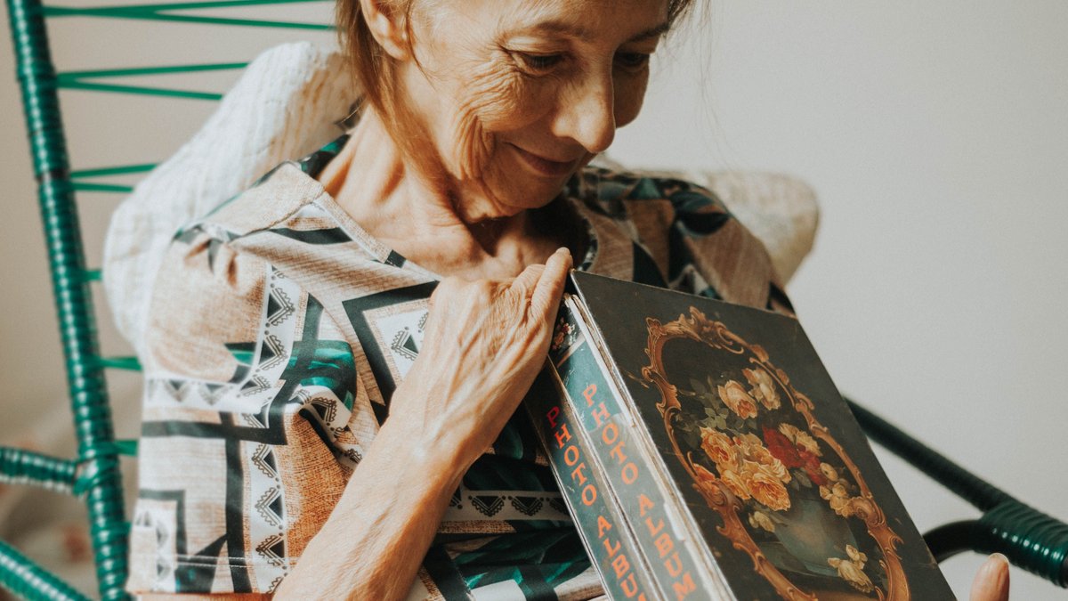 An elderly woman smiling warmly while holding a vintage photo album indoors.
