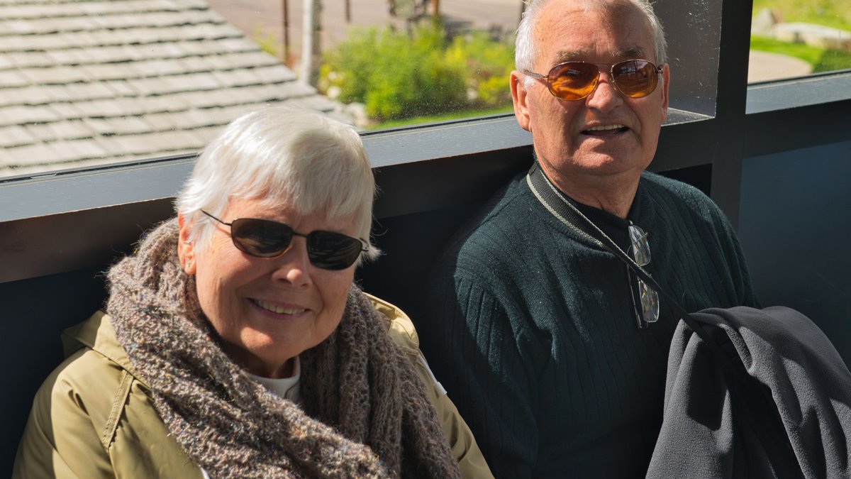 A happy senior couple wearing sunglasses and smiling, enjoying a sunny day outdoors.