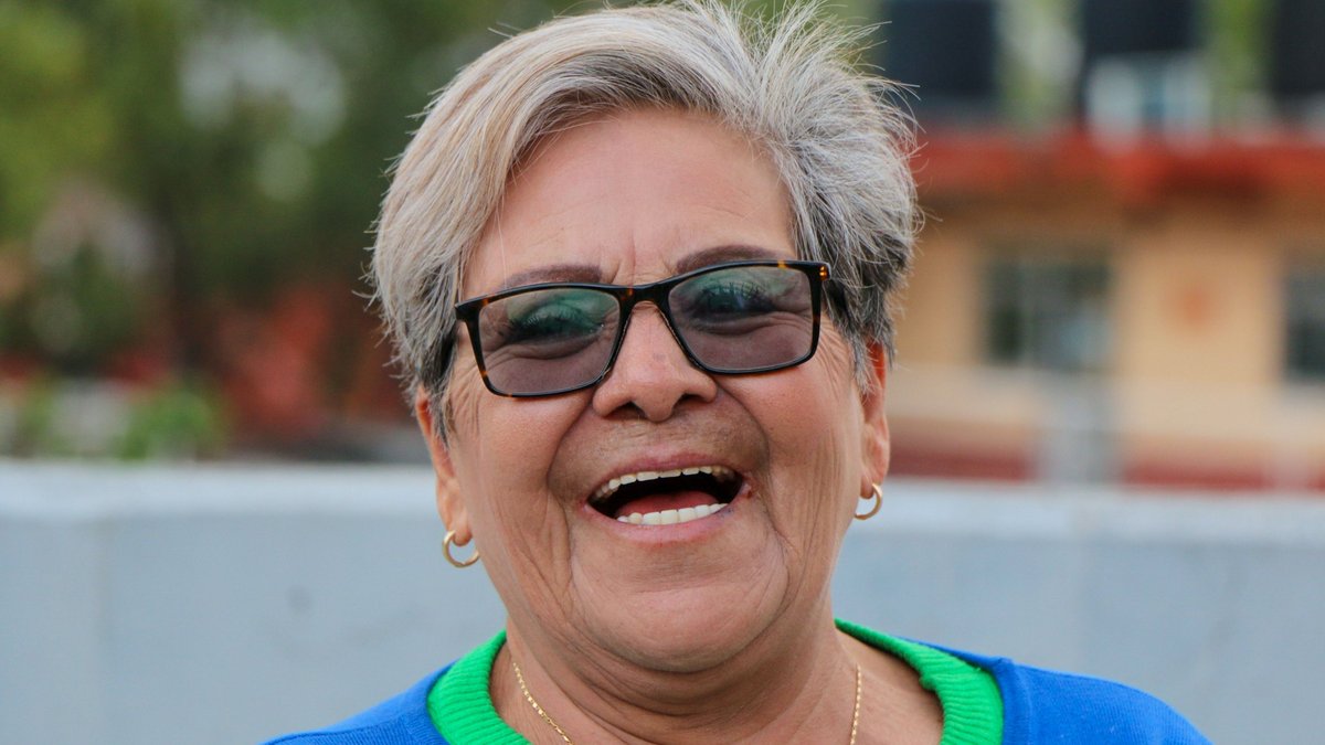 Portrait of a laughing senior woman wearing sunglasses and a blue top, enjoying a sunny day outdoors.