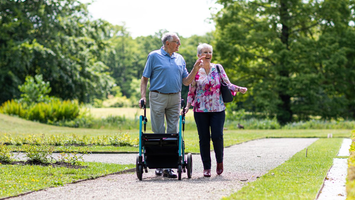 Senior couple walking in a park with a walker, enjoying a sunny day outdoors.