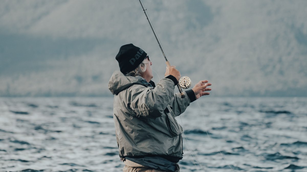 A senior man enjoys a relaxing day fishing on a mountain lake with a fishing rod.