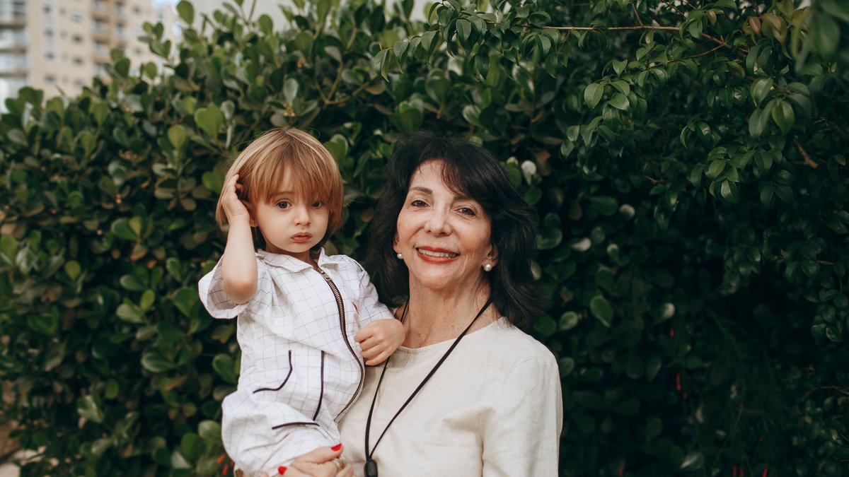 A loving grandmother with her grandchild smiling outdoors in a lush garden setting.