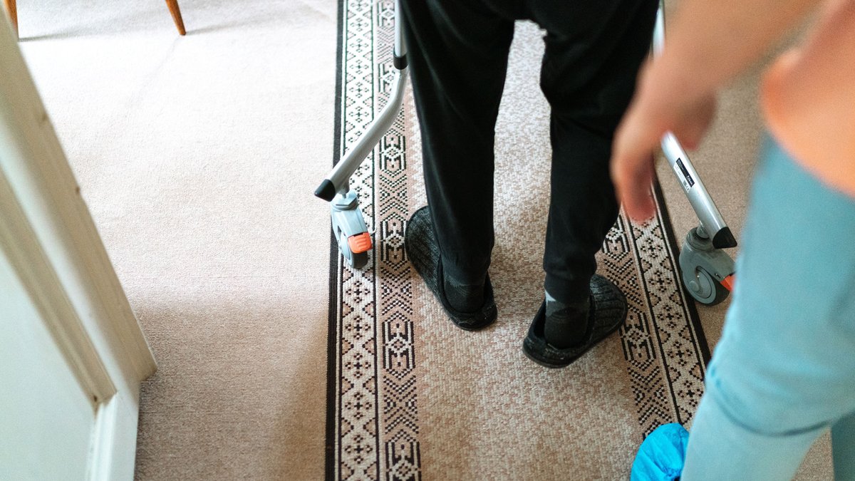 A senior person with a walker assisted by a caregiver in a cozy indoor setting.