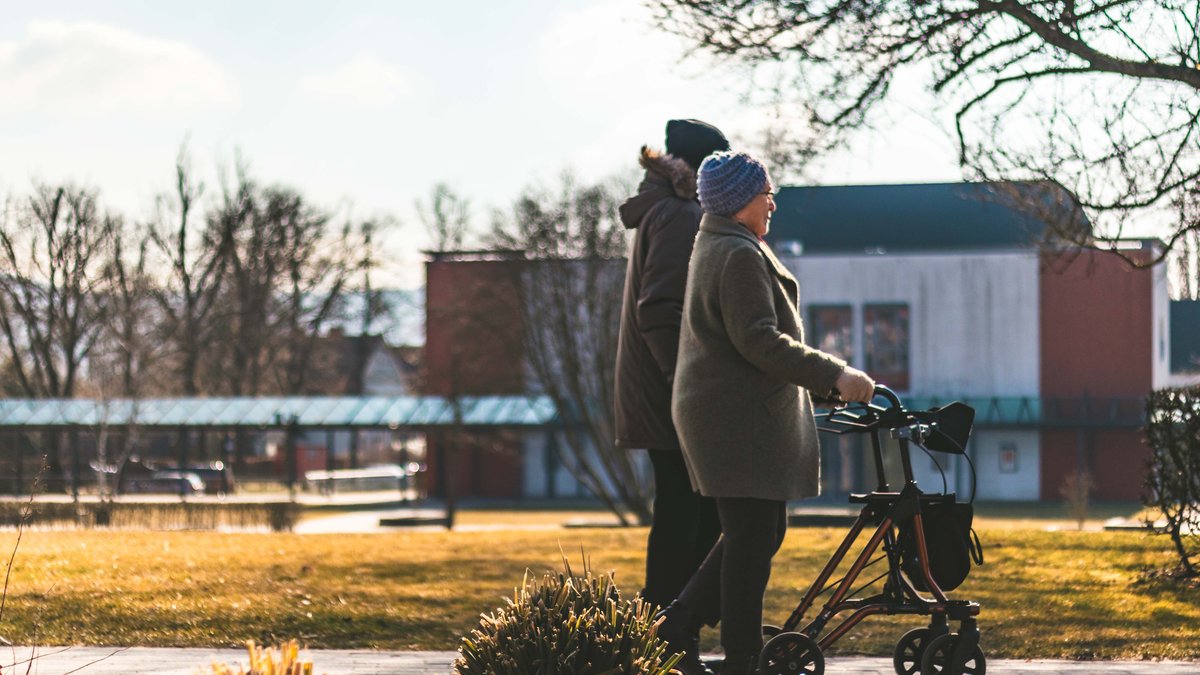 Two senior adults walking with a rollator in a sunny park on a crisp day.