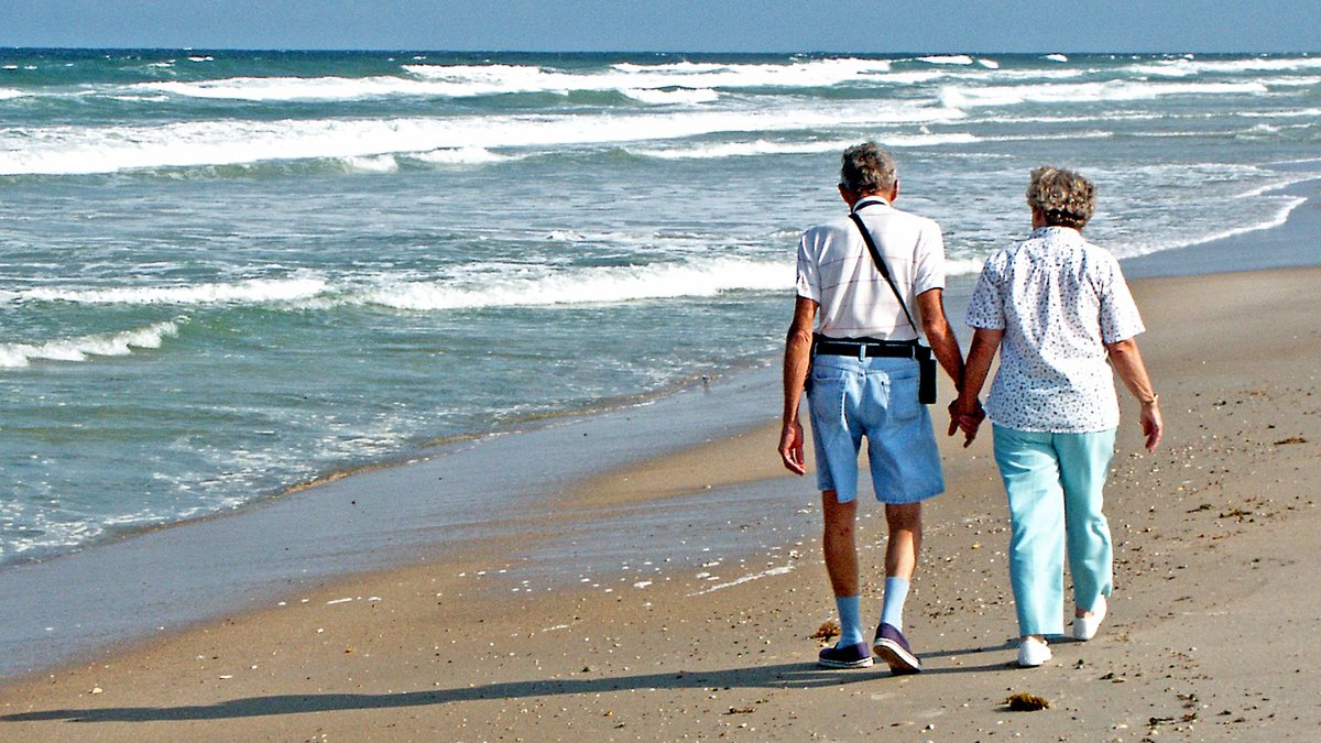 A senior couple enjoys a peaceful walk along the sunny Florida beach, hand in hand.