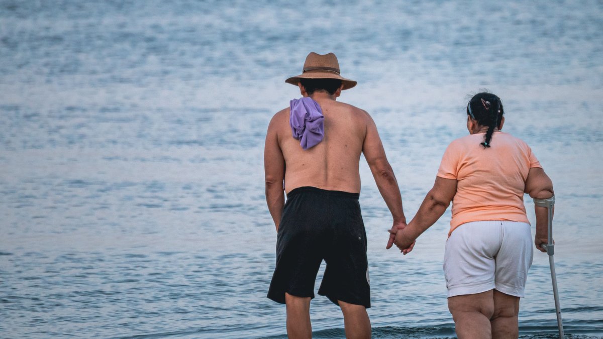 An elderly couple holding hands, enjoying a peaceful walk at the beach, symbolizing love and companionship.