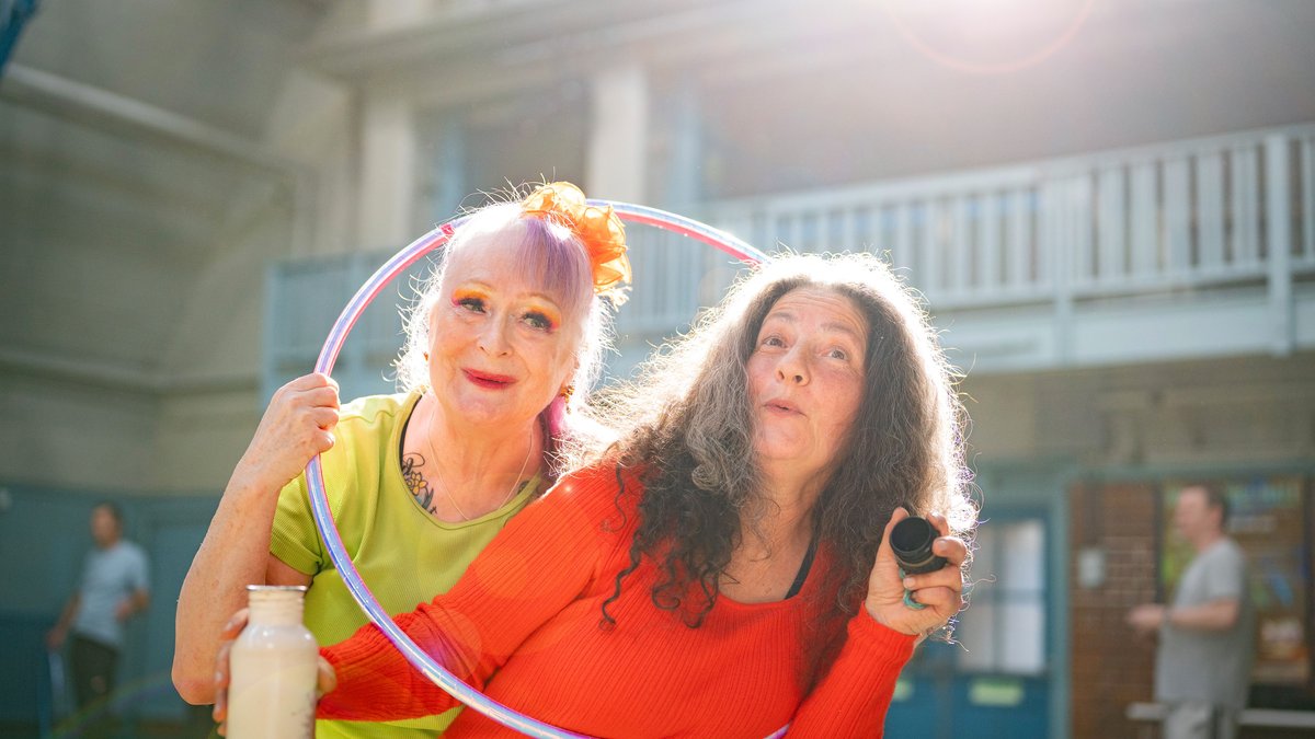 Two senior women enjoying a fun and lively exercise session with a hula hoop indoors.