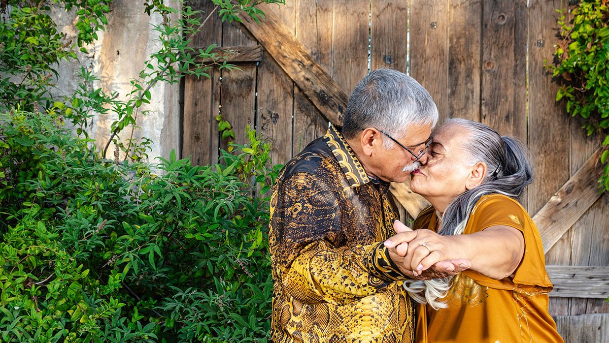 A joyful elderly couple shares a kiss and dances in a garden setting, exuding love and happiness.
