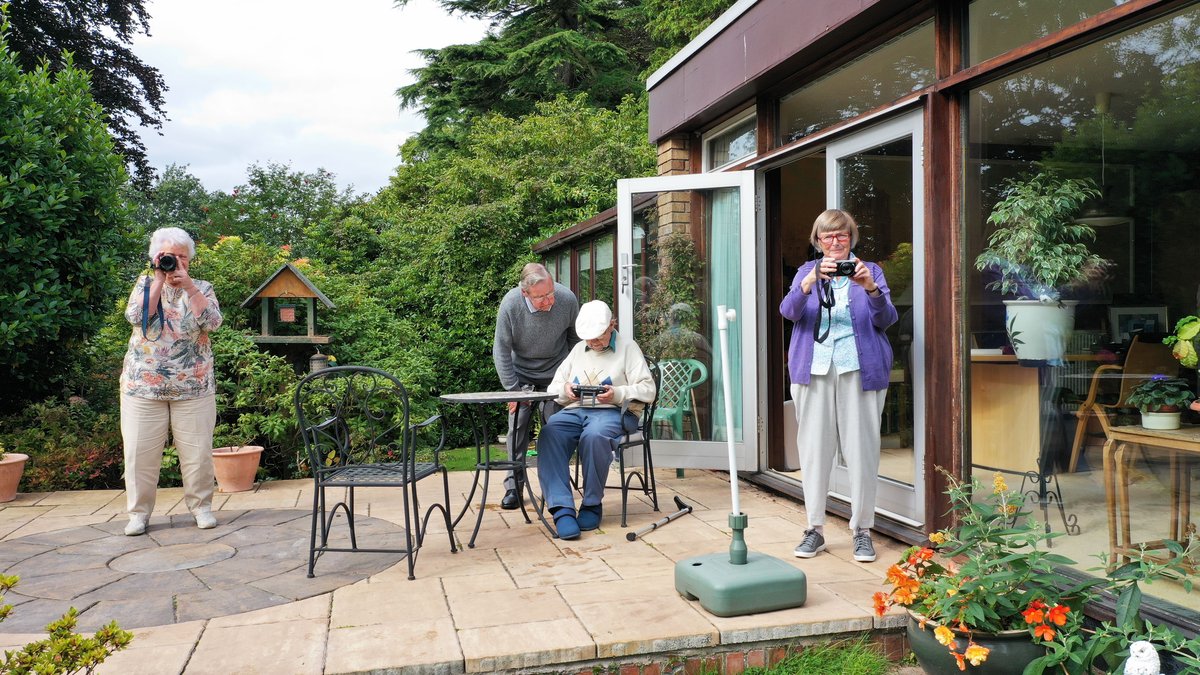 A group of senior adults taking photos in a garden on a sunny day.