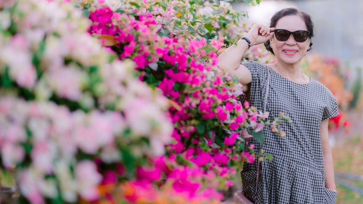 A joyful senior woman wearing sunglasses enjoys a sunny day in a colorful garden.