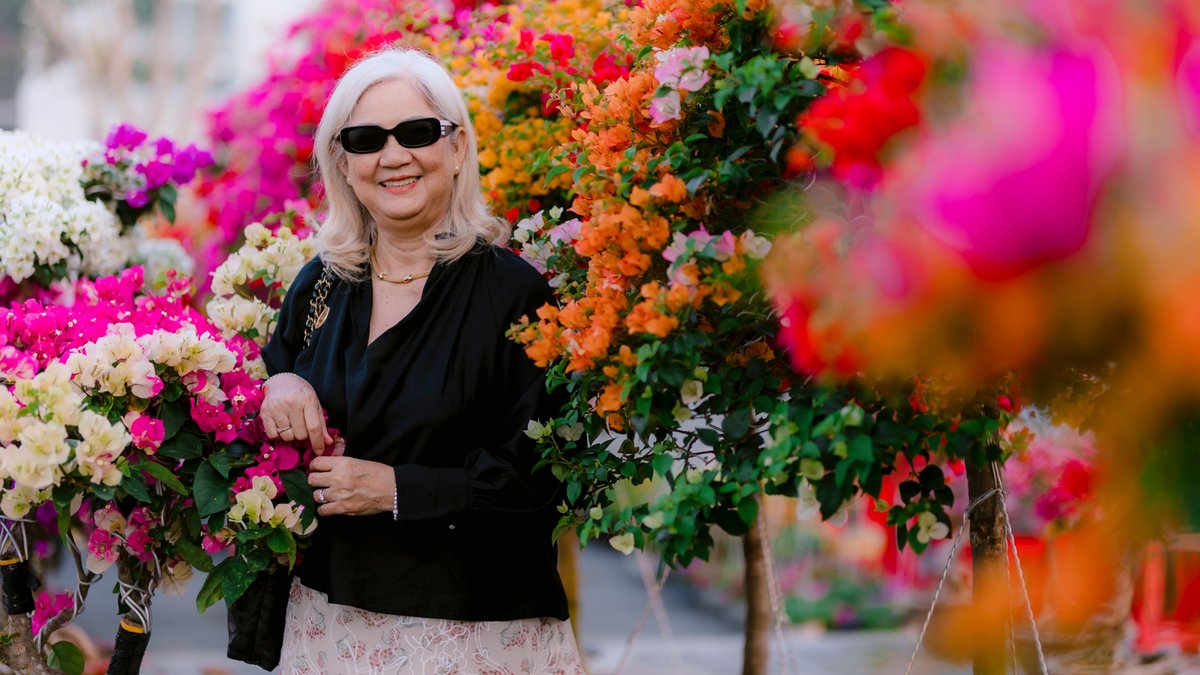 Senior woman in sunglasses enjoying a vibrant floral garden with colorful flowers around her.