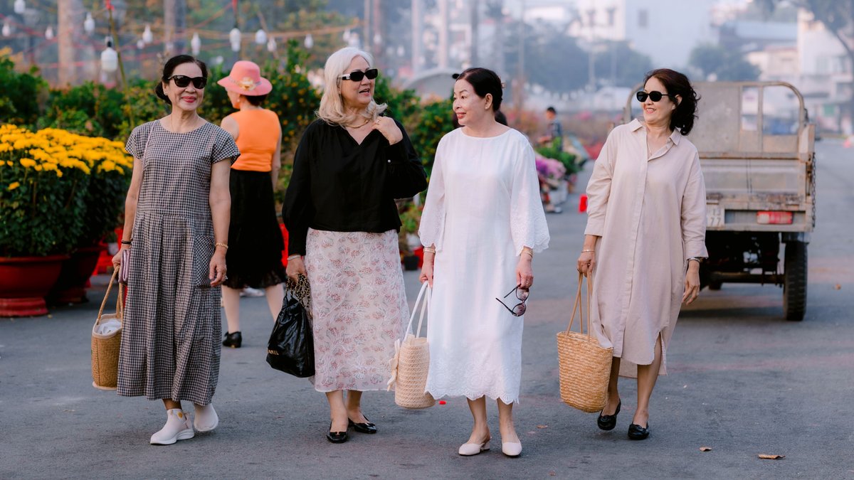 Four senior women enjoy a sunny day outdoors, chatting and walking with baskets.