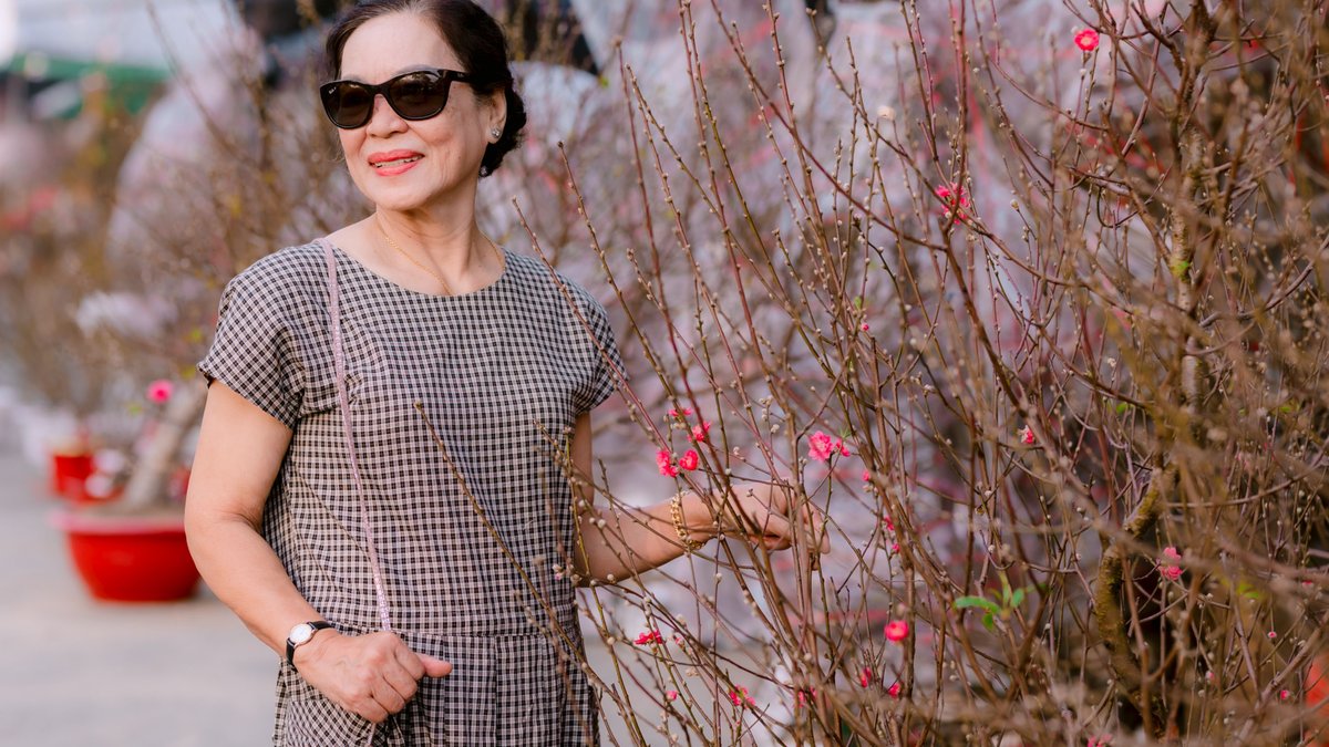Cheerful senior woman in sunglasses exploring a vibrant flower garden during spring.