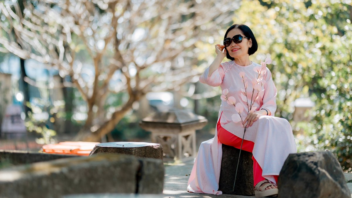 An elderly woman in a pink outfit and sunglasses enjoying a sunny day outdoors.
