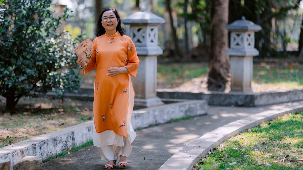 Senior woman wearing traditional attire walks gracefully in a serene garden.