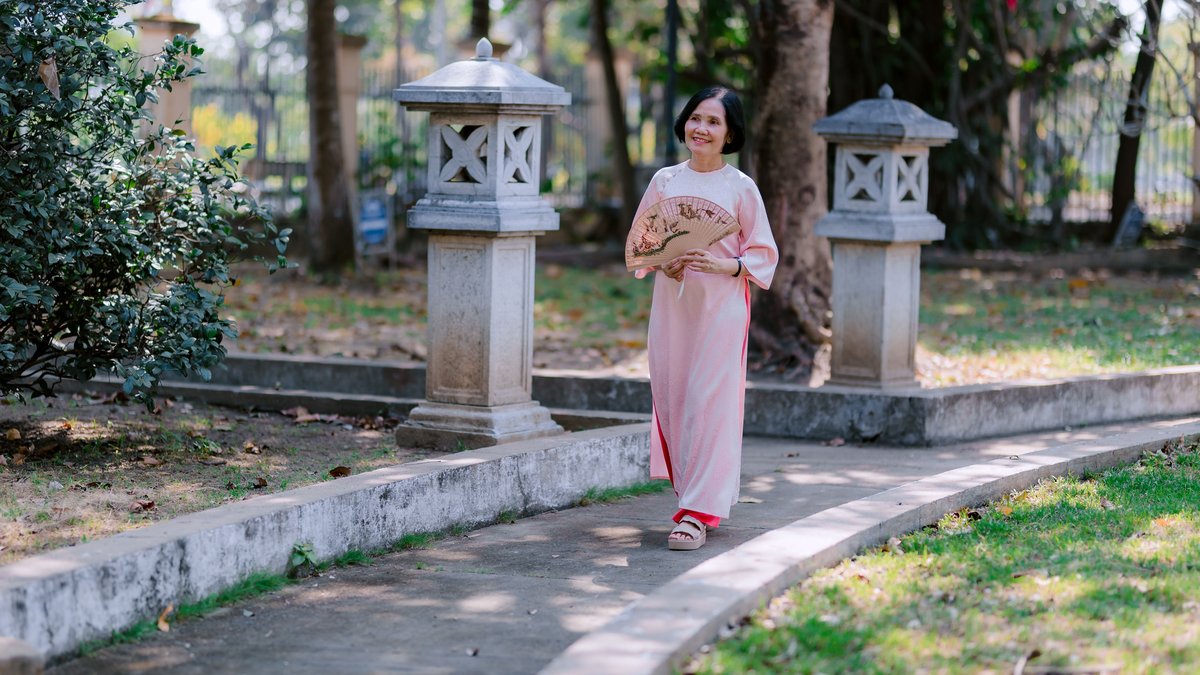 Elderly woman in traditional dress enjoys a peaceful walk in a sunny garden.