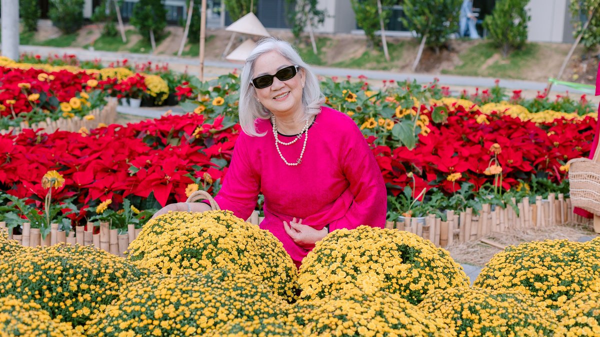 Senior woman in sunglasses smiling amidst colorful flower garden. Bright day outdoors.