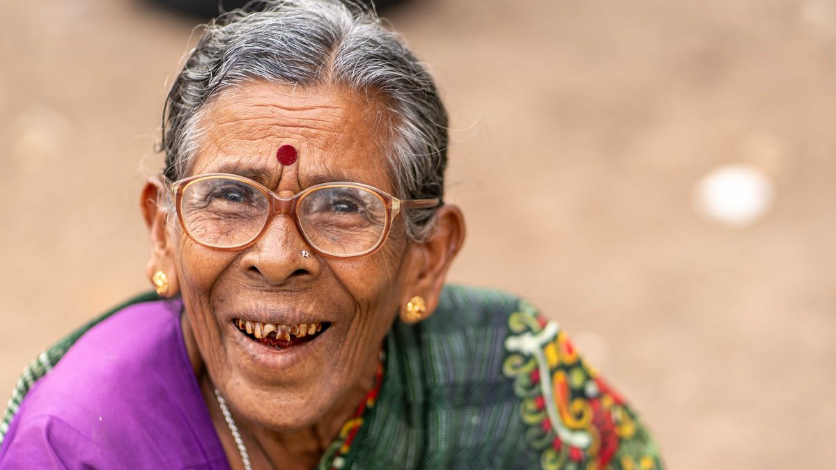 Portrait of a joyful senior woman wearing glasses and traditional attire, smiling outdoors.