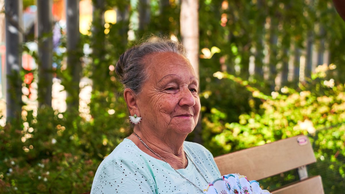 A senior woman enjoys a sunny day outdoors with a fan in San Sebastián de los Reyes, Spain.