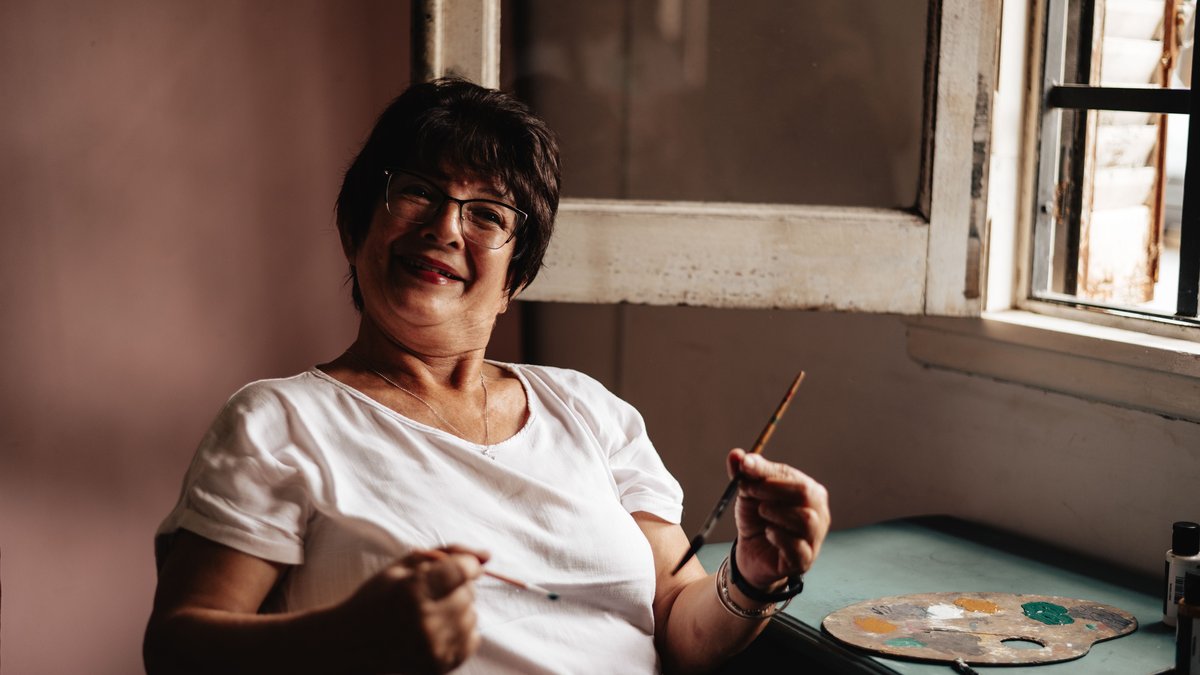 A joyful senior woman artist holding a paintbrush in her cozy Buenos Aires studio.