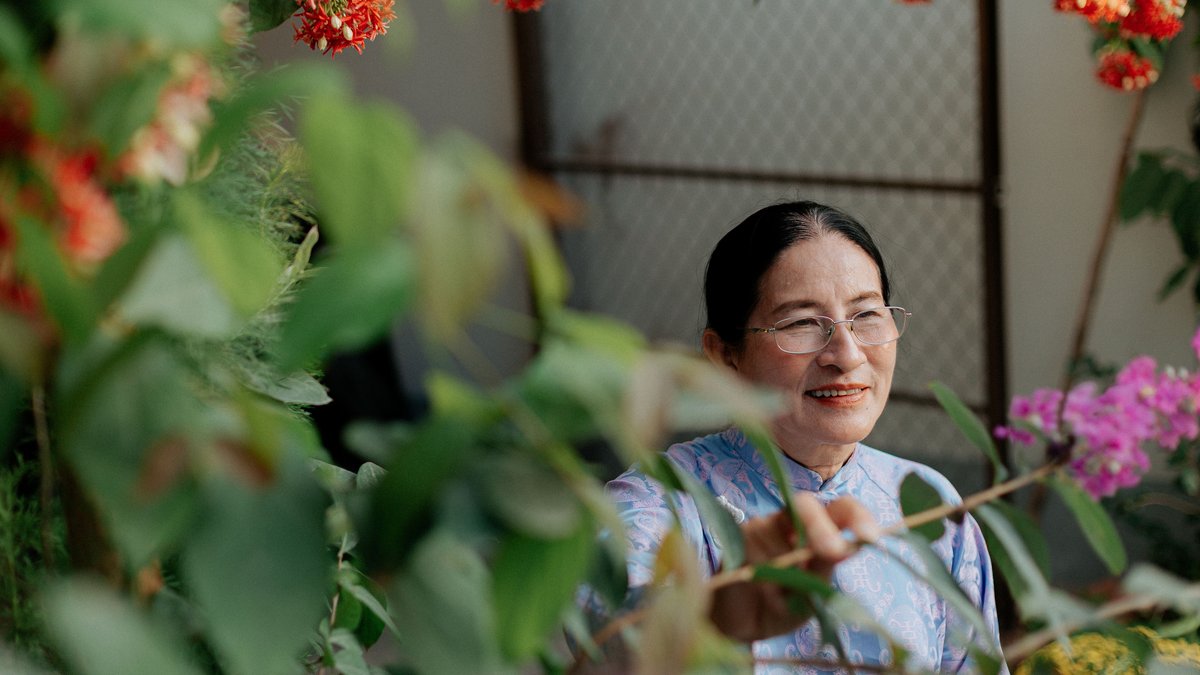 A senior woman enjoys colorful flowers in a vibrant garden setting.