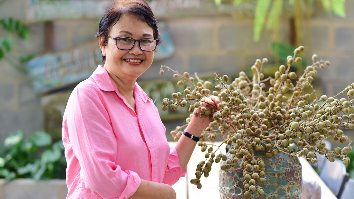 Smiling senior woman arranging indoor plants in a decorative vase, enjoying gardening.