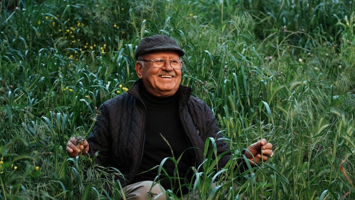 A senior man smiles amid lush greenery, embodying joy and tranquility in İstanbul's natural scenery.