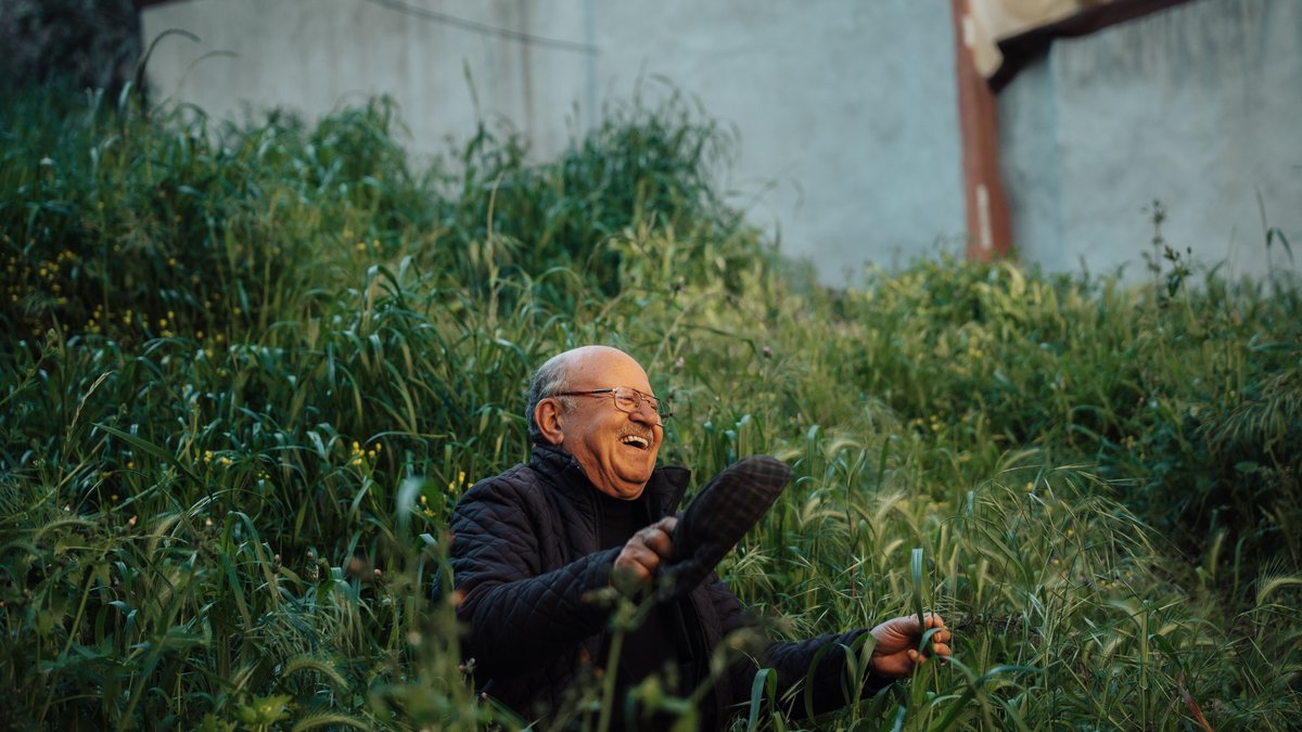 Cheerful elderly man enjoying a moment of laughter while sitting in a verdant garden.