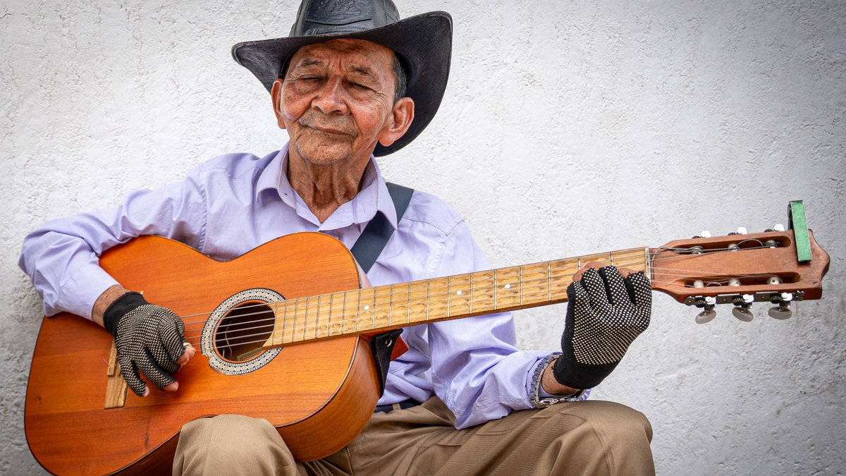 Senior man with a cowboy hat playing acoustic guitar outdoors, embodying a love for music.