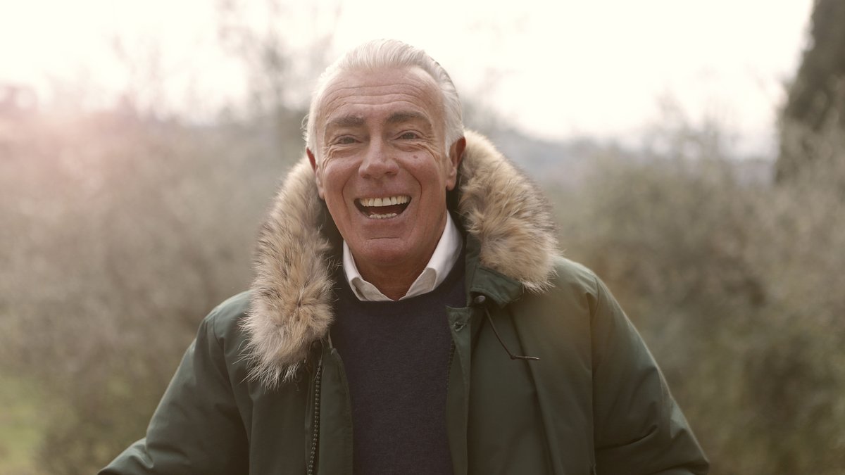 A smiling elderly man enjoying the outdoors in a fur-lined coat, exuding warmth and happiness.