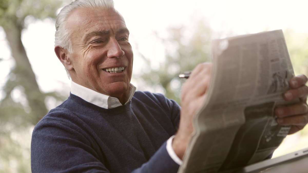 A happy senior man reading a newspaper outdoors, enjoying a sunny day.