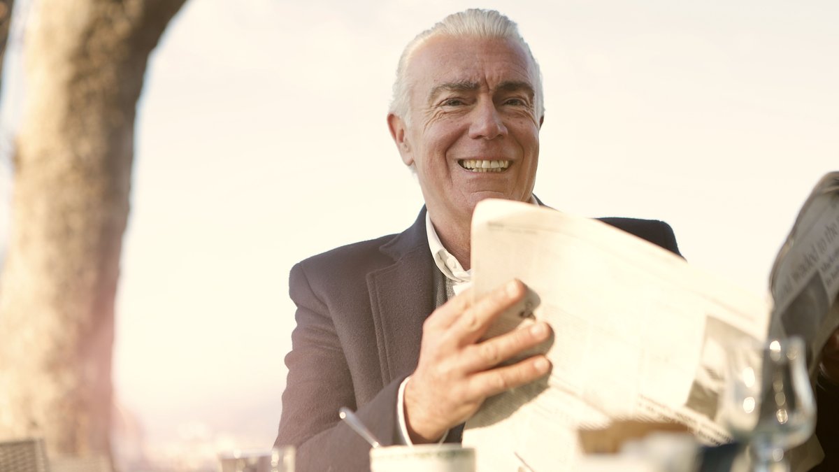 Elegant senior man enjoying a sunny day outdoors with coffee and newspaper.