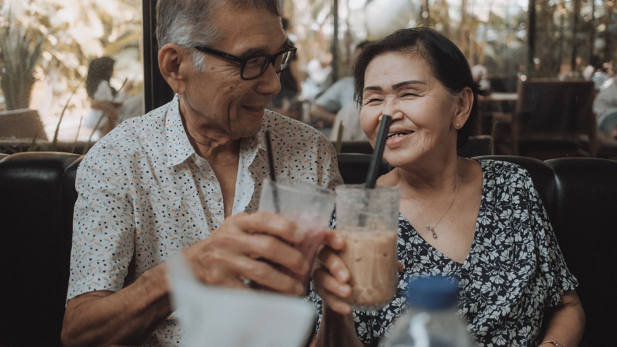 Happy senior couple sharing a moment with iced beverages in a cozy cafe setting.