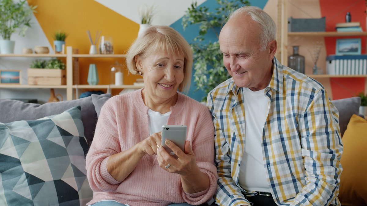 Happy senior couple using smartphone together in cozy living room, enjoying technology.