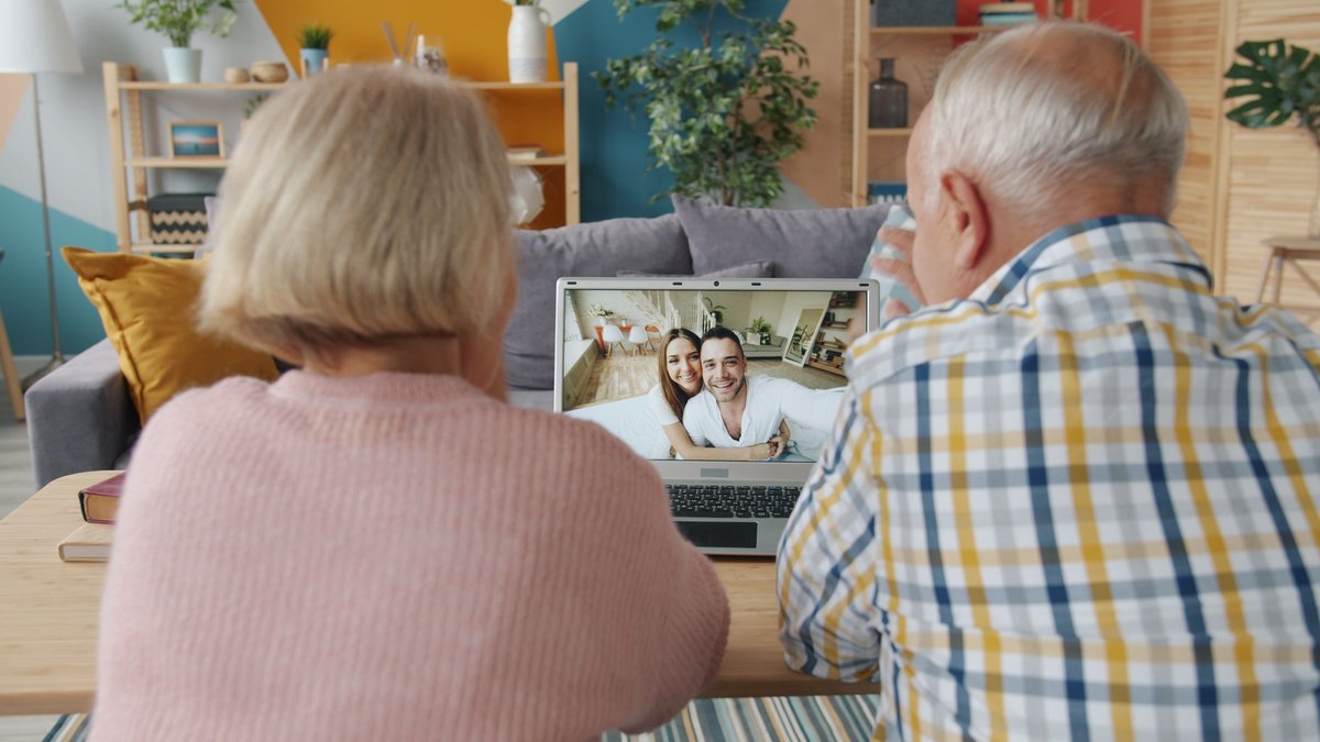 Senior couple enjoying a video call with family members on a laptop in a cozy living room.