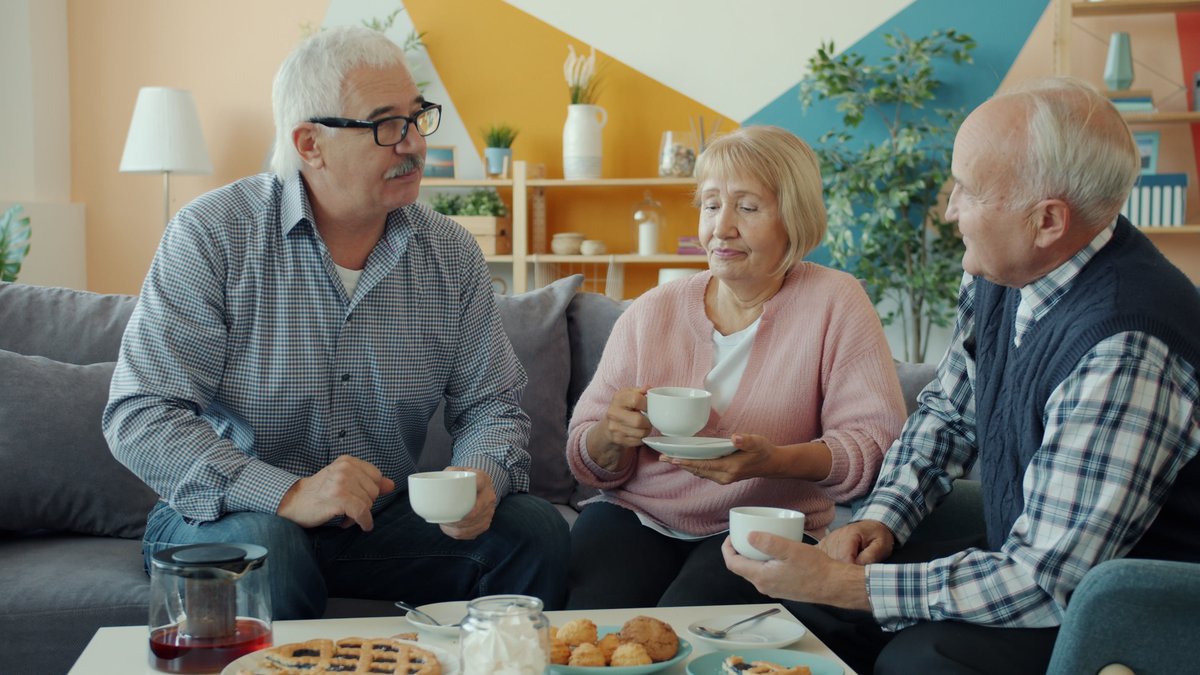 Three senior friends sharing coffee and conversation in a cozy living room setting.