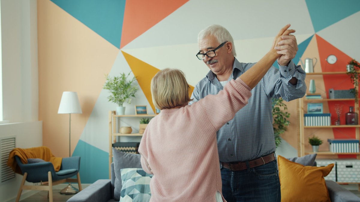 Senior couple enjoying a dance in a colorful, modern living room.