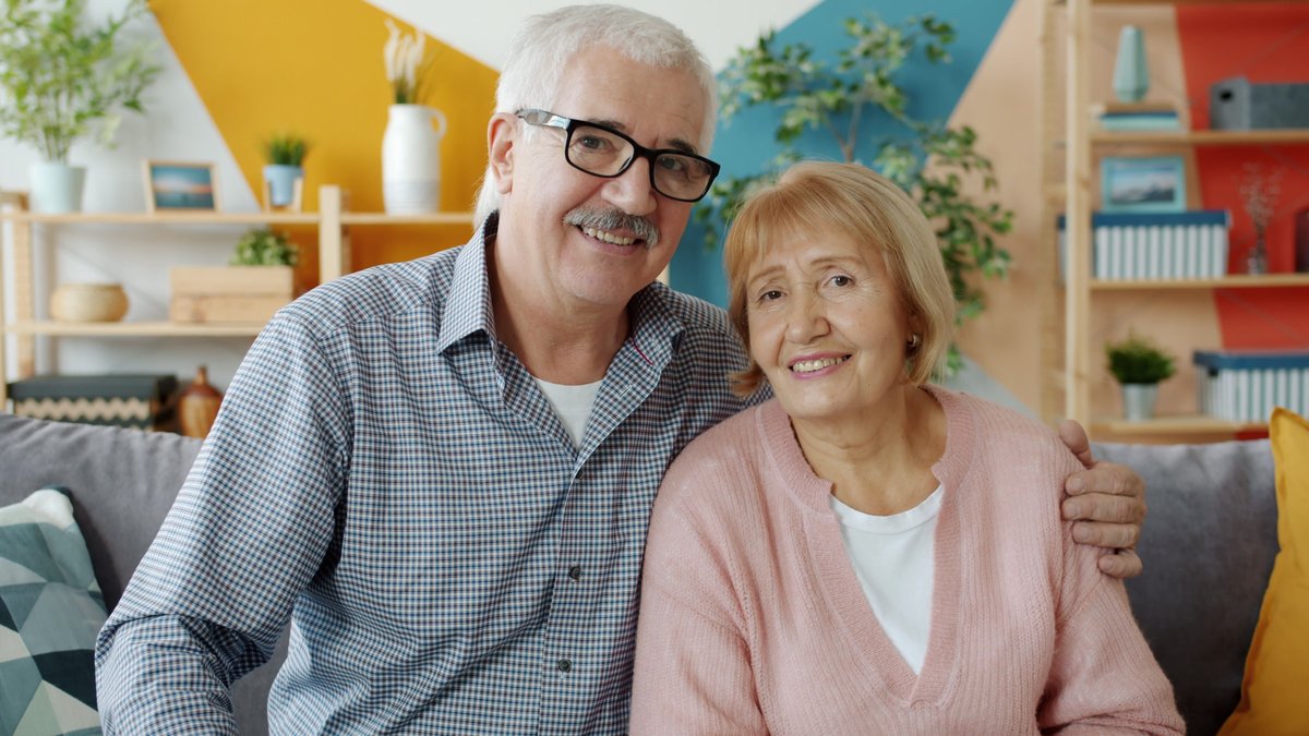 Smiling elder couple sitting together happily in a colorful living room.