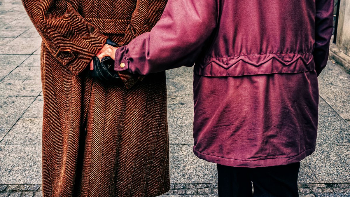 Elderly couple holding hands while walking on a sidewalk in Warsaw, symbolizing love and companionship.