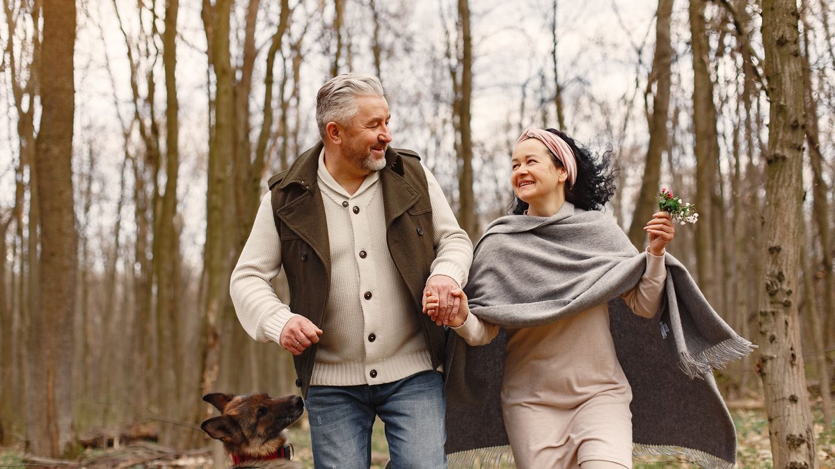 Joyful senior couple walking with their dog in a serene autumn forest, embracing love and nature.
