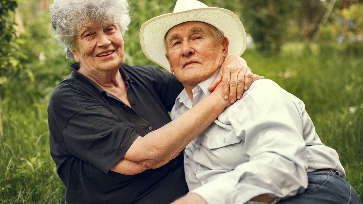 Happy elderly couple sitting together in a lush garden embracing and smiling.