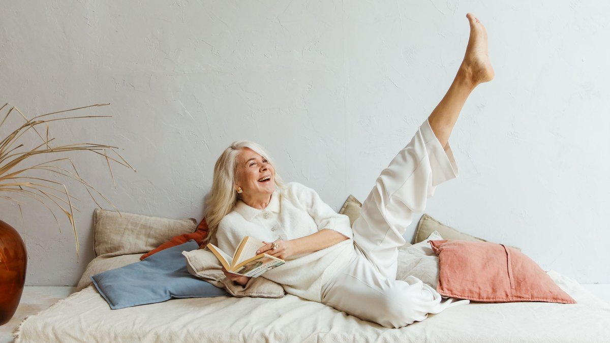 Joyful elderly woman relaxing indoors with a book, expressing carefree happiness.