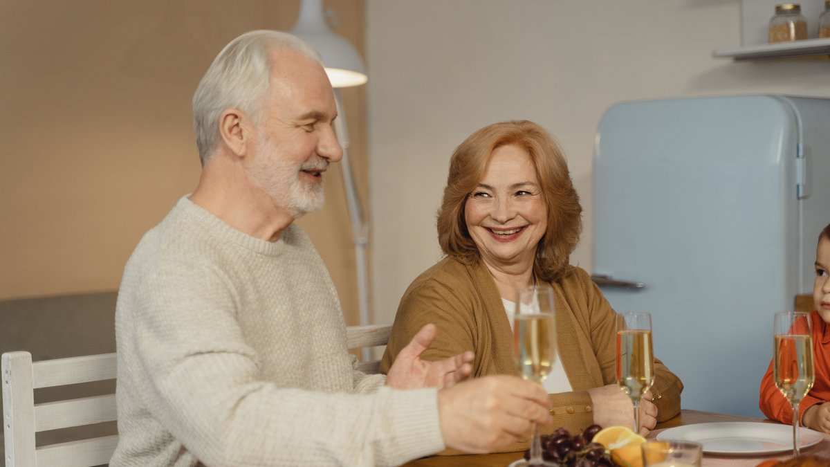 Elderly couple enjoying a joyful family dinner with champagne and fruit.