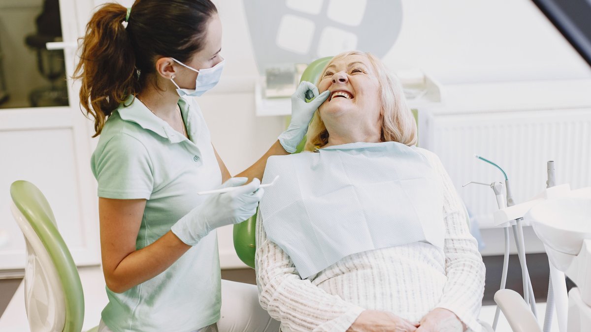 A female dentist examining a senior woman in a dental office. Both are smiling.