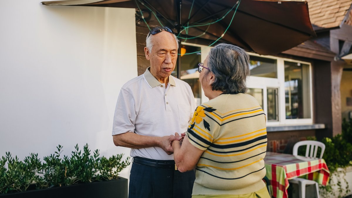 Senior Asian couple holding hands and expressing love and affection in a sunny outdoor setting.